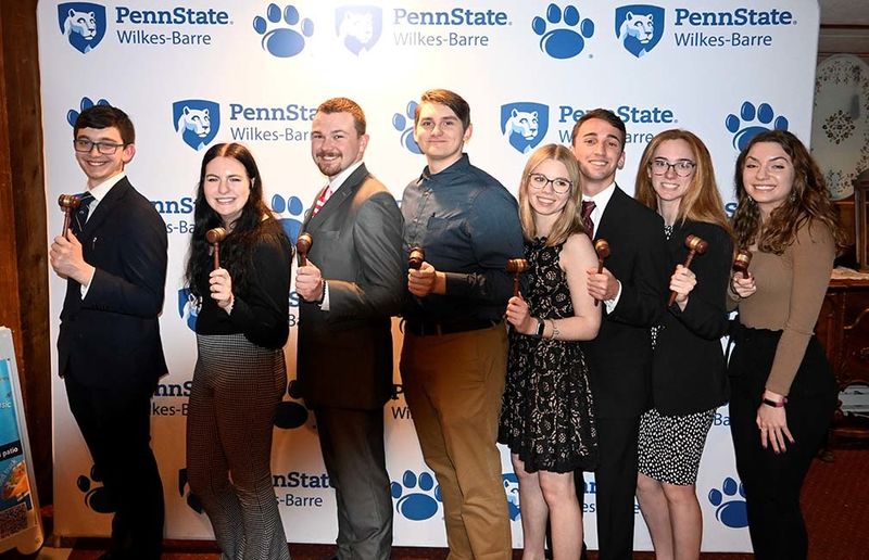 A group of students standing in front of a wall with Penn State Wilkes-Barre logos
