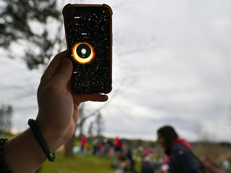 A hand holding up a cell phone using an app to track the eclipse.