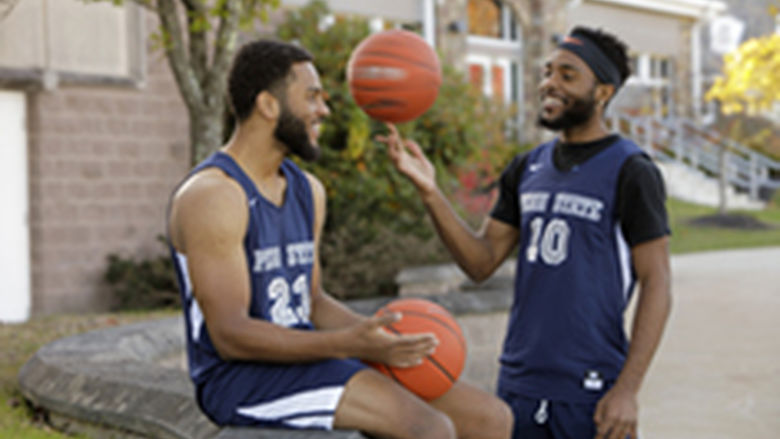Two Penn State Wilkes-Barre basketball players holding basketballs and conversing