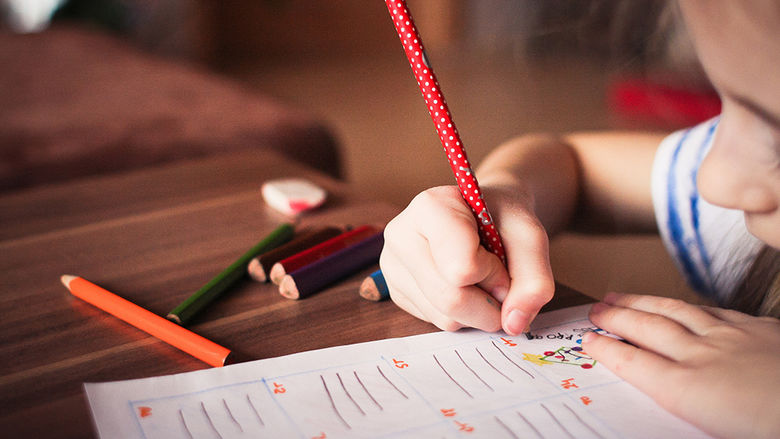 Small child at her desk in a classroom writing in pencil on a piece of paper