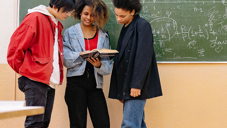 Three high school students gathered around a textbook