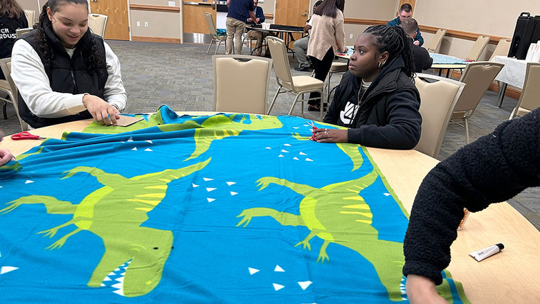 Students work on preparing a blanket laid out on a table.