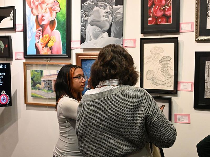 Two people talking while looking at a wall of gallery art.