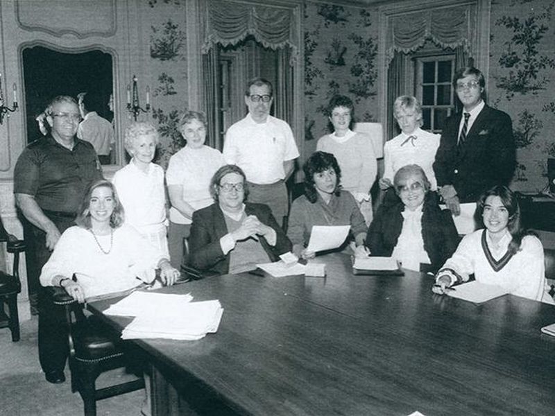 A black-and-white photo of a group of people seated at the edge of a table.