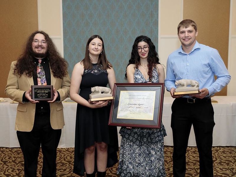 Four people standing alongside each other indoors, holding individual awards.