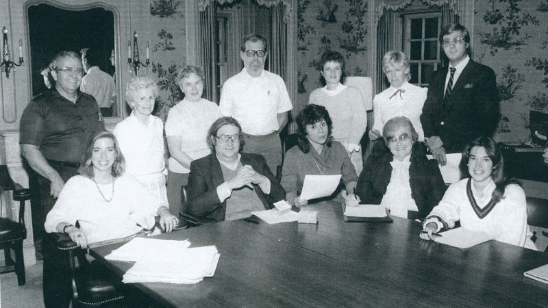 A black-and-white photo of a group of people around a table.