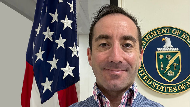 John Krohn standing in front of an American flag and the seal of the Department of Energy