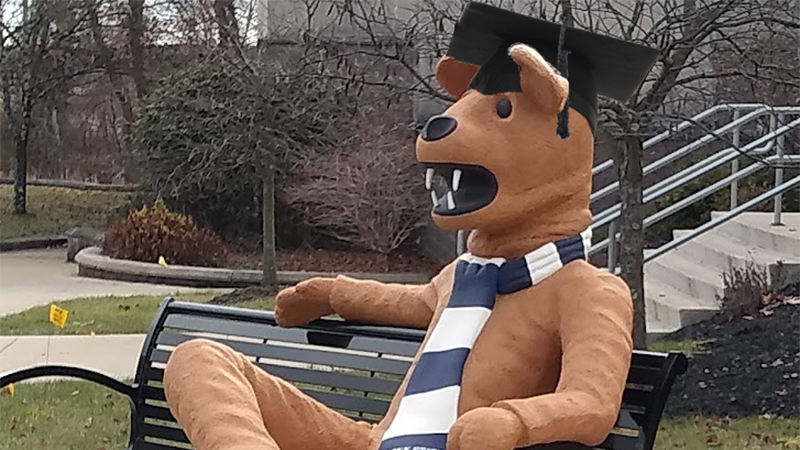 Nittany Lion statue wearing a mortarboard and sitting on a bench in front of the Struthers Career Services Center