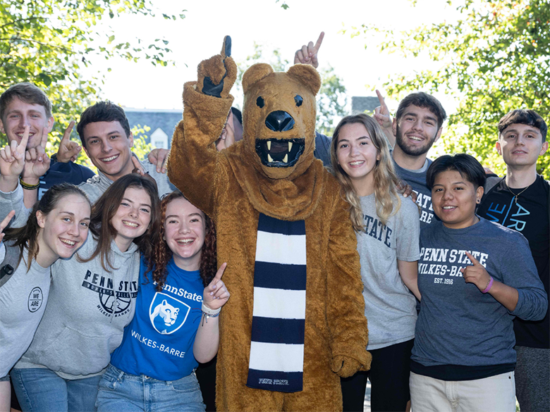 Nittany Lion mascot with students gathered together for photo. They are all holding up their index fingers to indicate "We're number 1!"