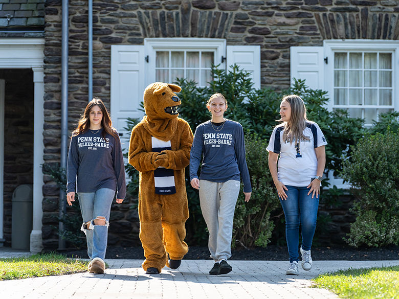 The Nittany Lion mascot walking with three students in front of Hayfield House on the Penn State Wilkes-Barre campus