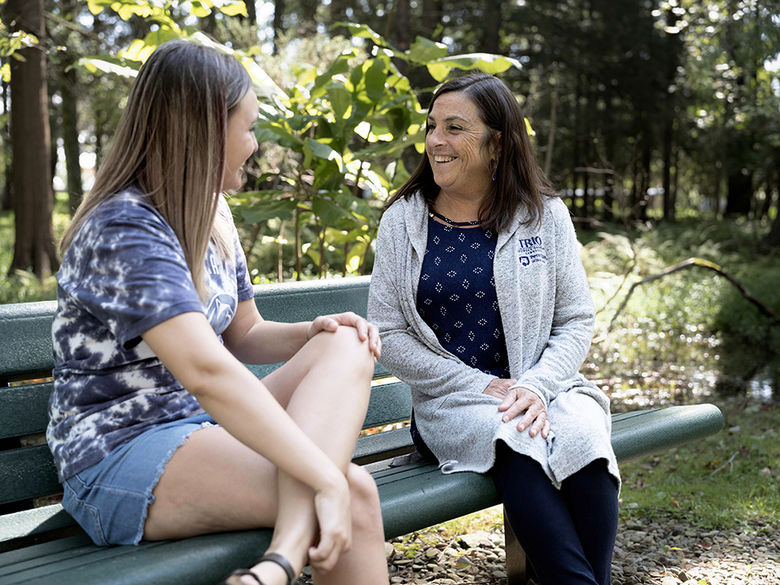 A student chatting with an advisor on a sunny bench on campus