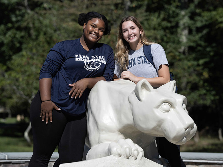 Two women students, one black and the other white, standing together at the Nittany Lion shrine statue on campus
