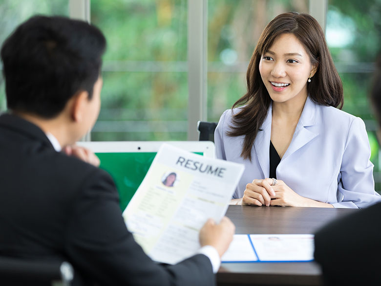 A young Asian woman facing the camera who is interviewing with someone who's back is to the camera