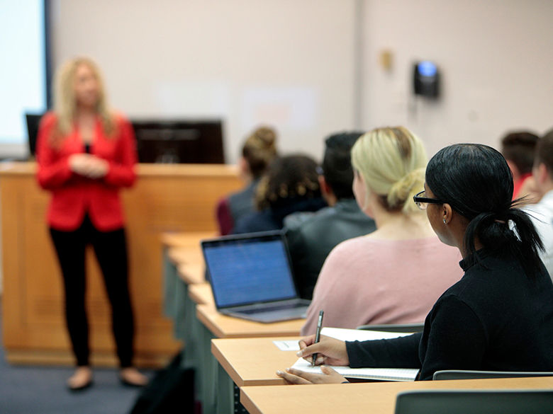 Professor in front of class in a bright red top