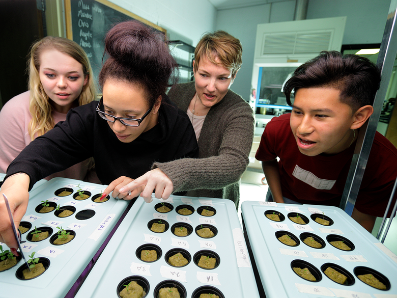 diverse students examining plants in biology lab with female professor