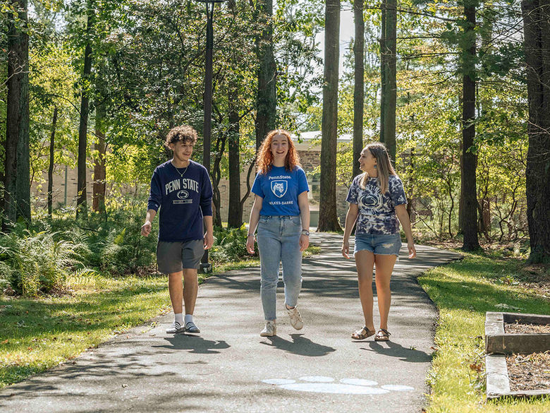 Three students strolling down a wooded path on campus