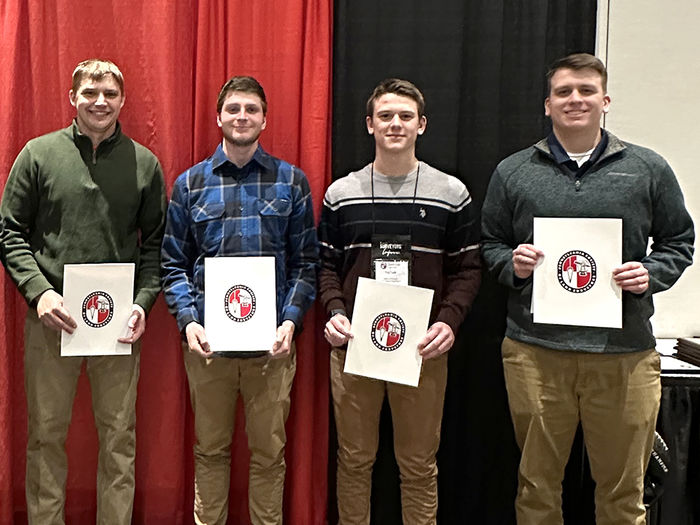 Four men standing holding certificates in honor of the scholarships they received.