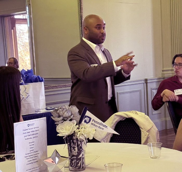 A man standing aside a table gestures while speaking.