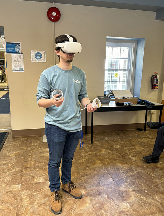 A man standing and wearing a pair of virtual reality goggles, with controllers on each hand.