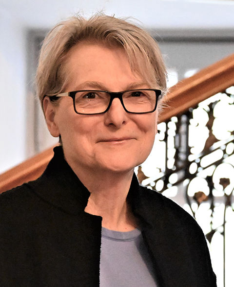 Lynda Goldstein, chancellor, standing in front of circular floating staircase in Hayfield House