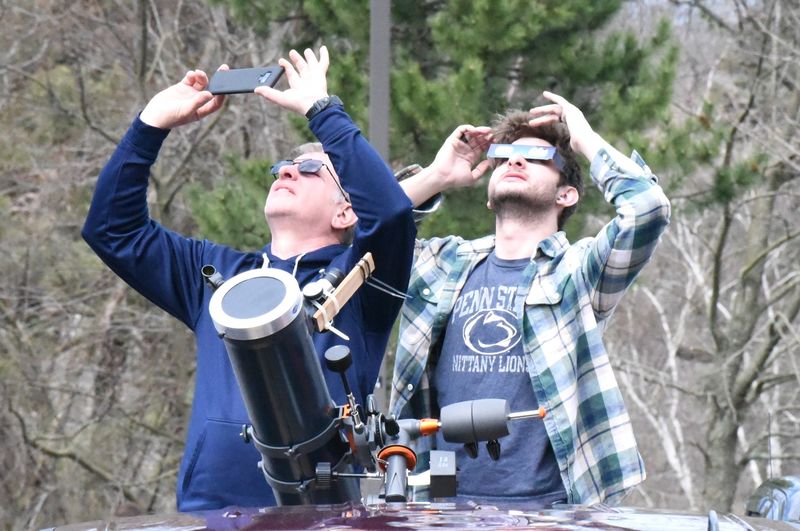 Two people with telescopes looking up at eclipse