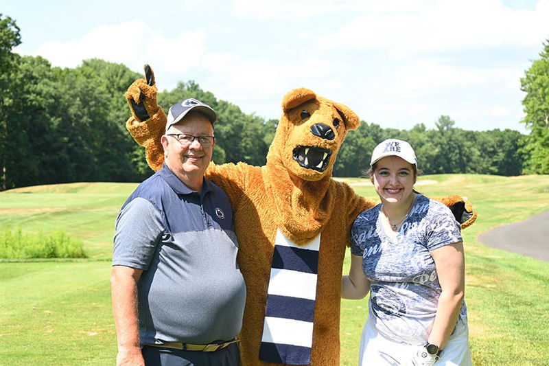 Two people standing with the Nittany Lion.