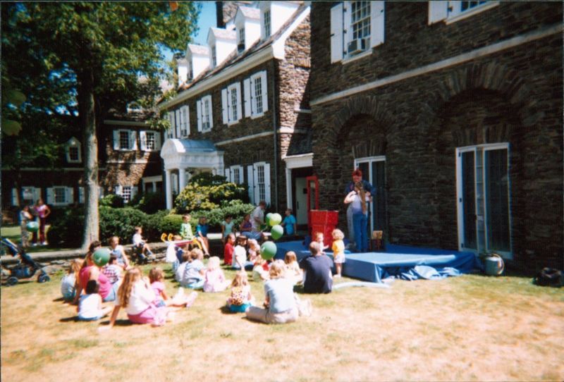 Children watching someone make balloon art outdoors.