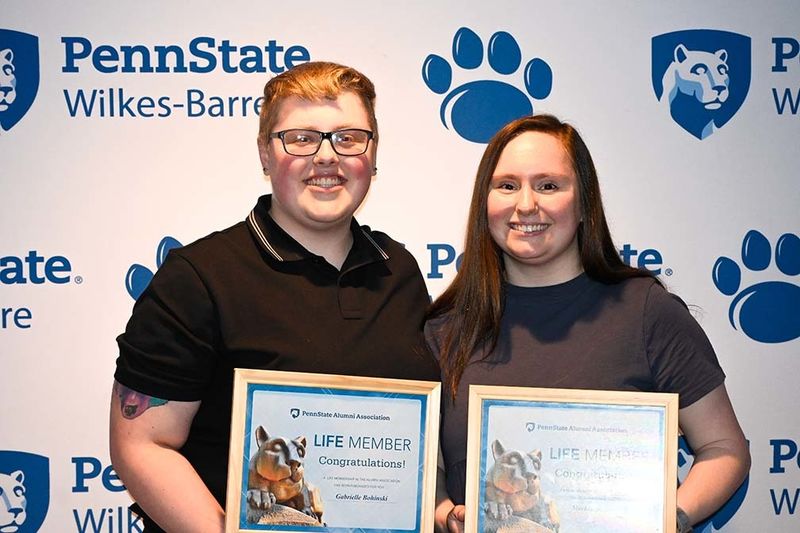 Two students standing with awards against a wall with Penn State Wilkes-Barre logos