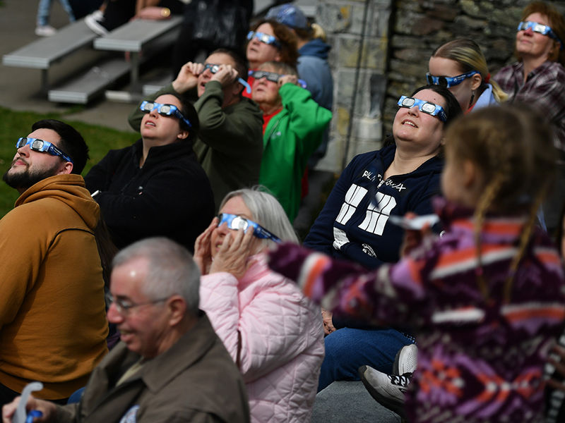 People sitting outside and looking at the sky wearing eclipse glasses.