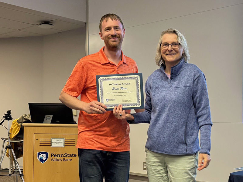 A man at left receives an award from a woman at right.