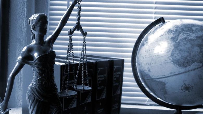 Lady Justice holding scales next to a globe placed on a desk.