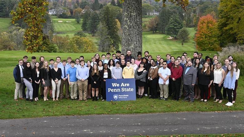 A large group of students standing outdoors with a sign that says We Are Penn State