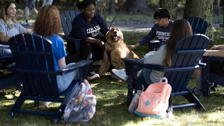 Four students seated in chairs with a dog in the circle.