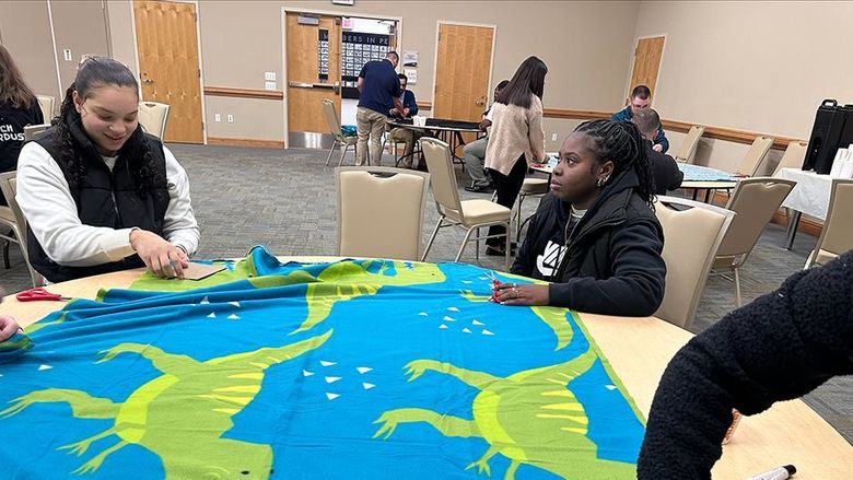 Students work on preparing a blanket laid out on a table.