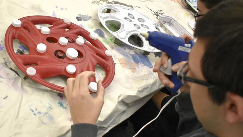 A student paints a hubcup red.