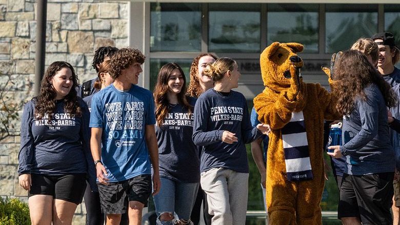 A group of students interacting with the Nittany Lion mascot outdoors.