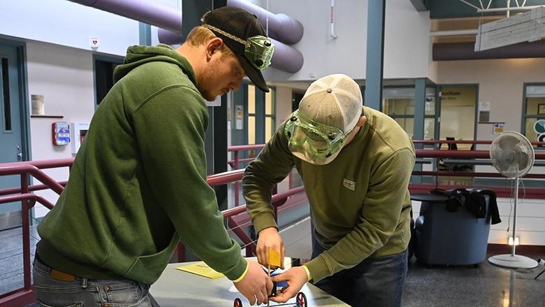 Two students work on a project on a table.