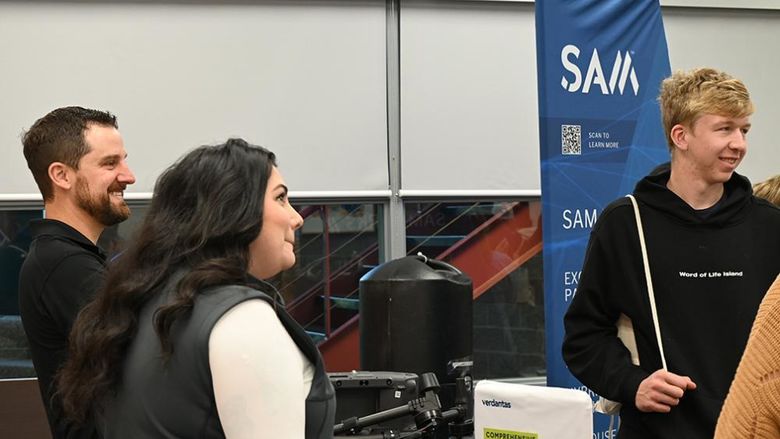 Adults and students conversing during a career fair, with a flag with the SAM logo at back right.