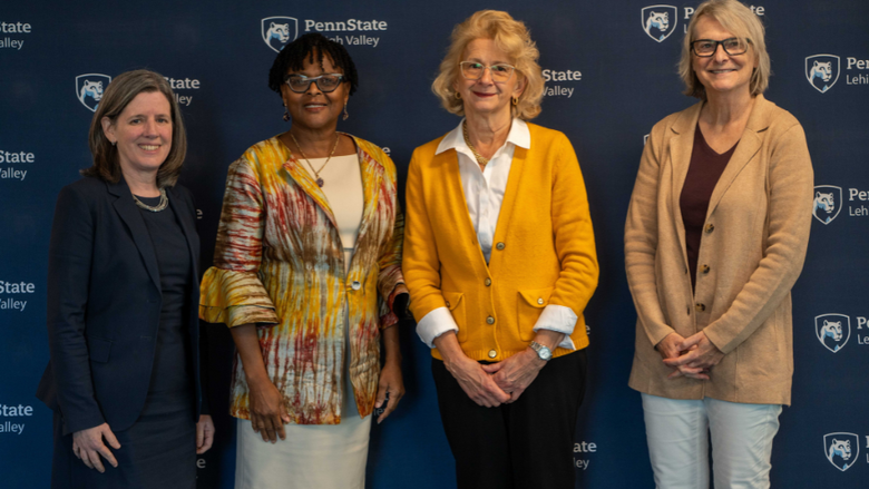 four women smile in front of a penn state step and repeat backdrop