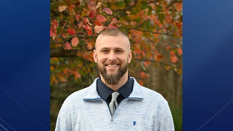 A man standing outdoors in front of a tree with fall-colored leaves.