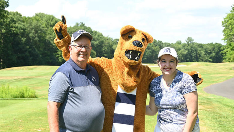 Two people standing with the Nittany Lion.