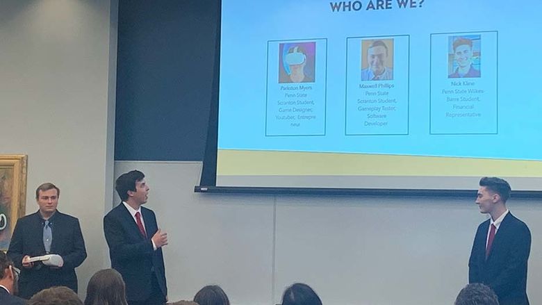 Three students with a PowerPoint presentation projected behind them.