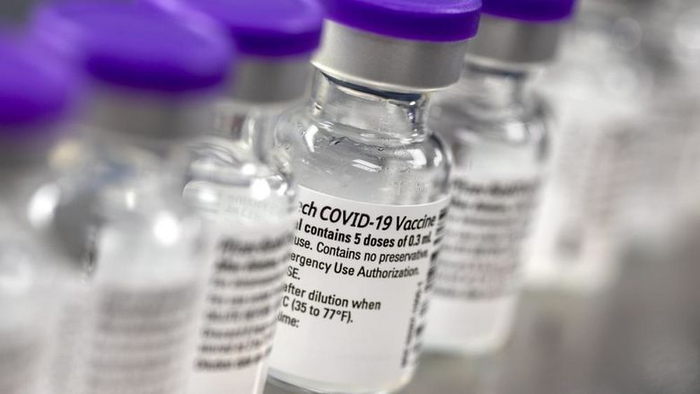 A row of vials show labels indicating they contain the COVID-19 vaccine.