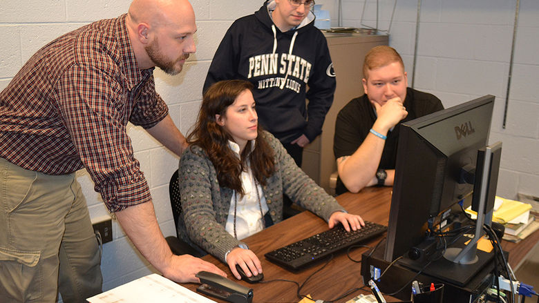 students and faculty gathered around a computer monitor examining the contents of the display