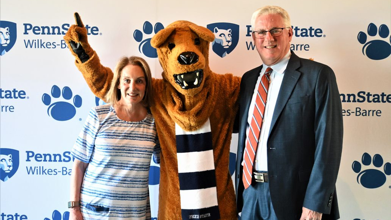 Two people standing with the Nittany Lion between them.