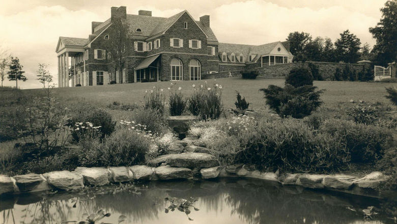 A stone mansion with a pond in the foreground