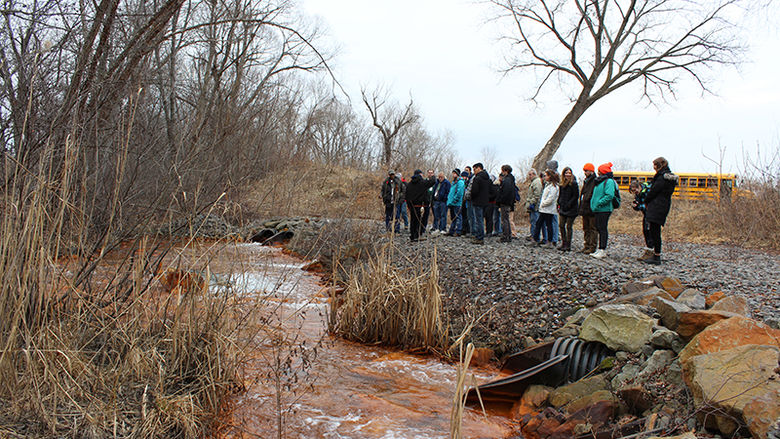 Students looking at a creek filled with brown sediment during a tour of Brownfields