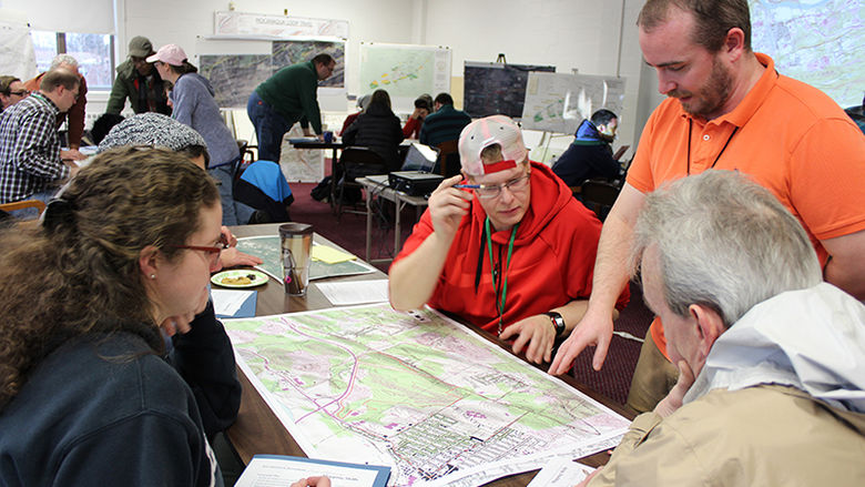 Students in a classroom gathered around a surveying map as the instructor points out an item of interest