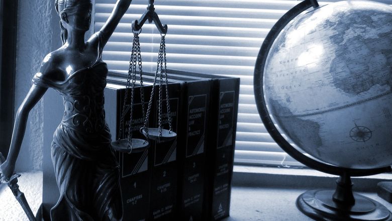 Lady Justice holding scales next to a globe placed on a desk.