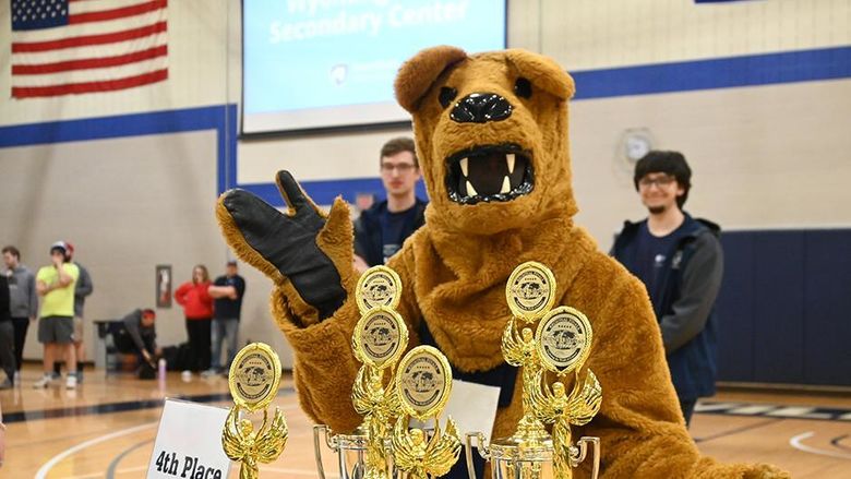 The Nittany Lion standing behind a table of trophies.